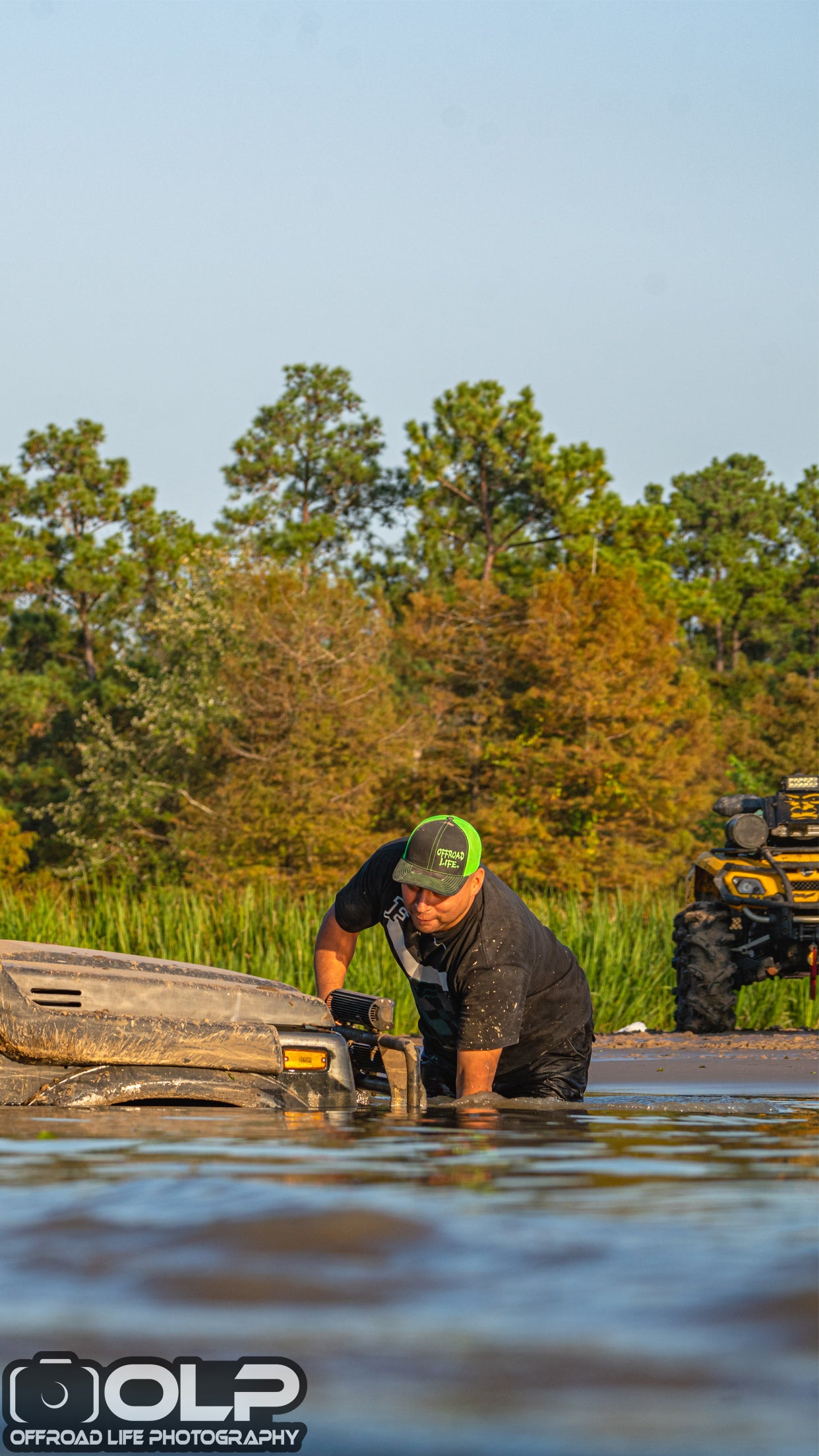 Person connecting tow rope in a shallow water area with trees and atv in the background